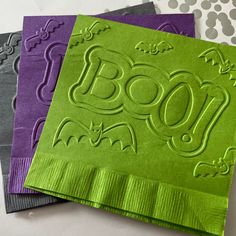 three napkins with the word boo printed on them, one in purple and one in green