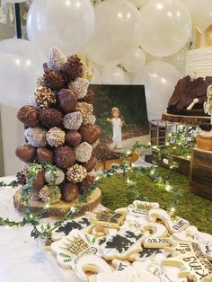 a table topped with lots of chocolate covered cookies and pretzels next to white balloons