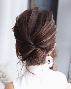 a woman with brown hair wearing earrings and a white dress is looking at herself in the mirror