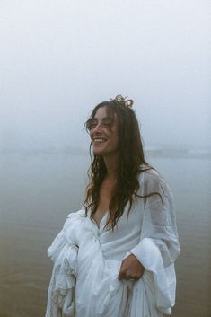 a woman with long hair standing in front of the ocean on a foggy day