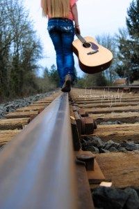 a woman walking on train tracks with a guitar