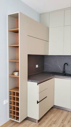 an empty kitchen with wooden floors and white cabinets in the corner, next to a wine rack