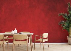 a dining room table with chairs and a potted plant in front of a red wall