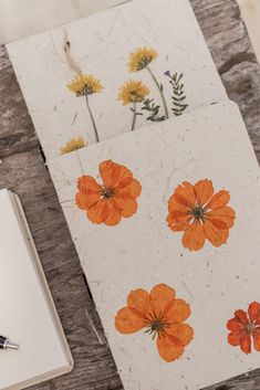 an open notebook with orange flowers on it next to a pen and paper clipping