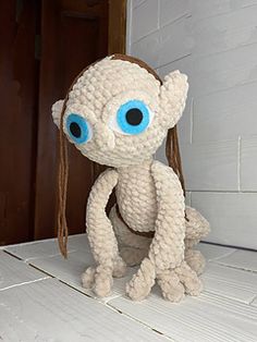 a stuffed animal with big blue eyes sitting on the floor next to a wooden door