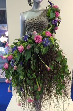 a mannequin is covered in flowers and greenery as it stands on display