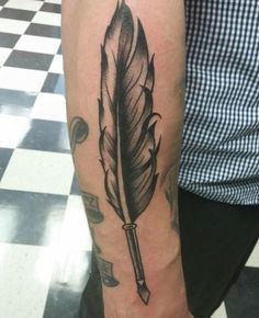 a man with a tattoo on his arm holding a pen and feather quill in it