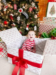 a baby sitting in a gift box under a christmas tree