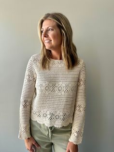 a woman standing in front of a wall wearing a white sweater and khaki pants