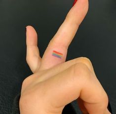 a woman's finger with a small rainbow tattoo on it