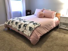 a bed with pink sheets and pillows in a bedroom next to a white night stand