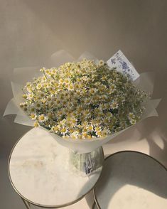 a bouquet of daisies in a glass vase on a white table with two plates