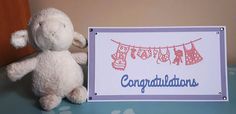 a white stuffed animal next to a congratulations card with clothes hanging on the clothesline