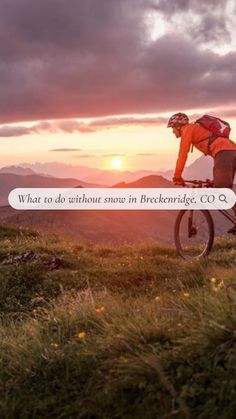 a man riding a bike on top of a lush green hillside under a cloudy sky