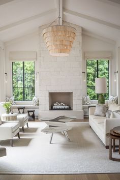 a living room with white furniture and a chandelier hanging from the ceiling in front of a fire place