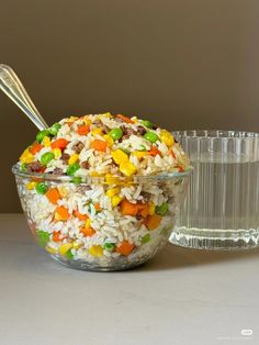 a glass bowl filled with rice and veggies next to a plastic container full of water