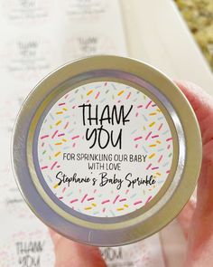 a hand holding a small tin with sprinkles on it that says, thank you for sparkling our baby with love