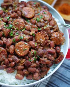 a white bowl filled with rice covered in sausage and beans on top of a table