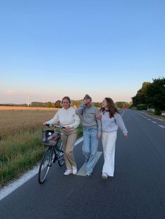 three people are walking down the road with a bike in front of them and one person is standing next to her