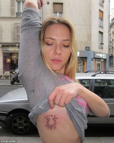 a woman with a tattoo on her stomach is looking down at the ground in front of a car