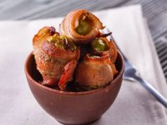 a bowl filled with meat wrapped in bacon and jalapenos next to a fork