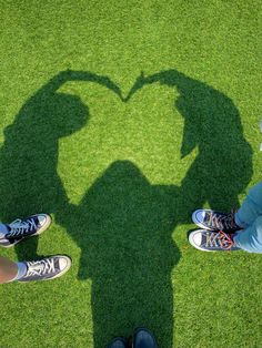 two people standing in the shape of a heart with their shadows on grass behind them