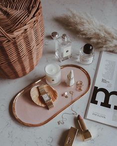 an assortment of beauty products on a tray next to a basket and perfume bottle in the background