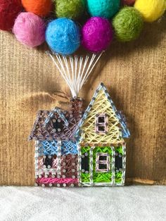 two small houses made out of plastic and yarn with colorful balls in the air above them