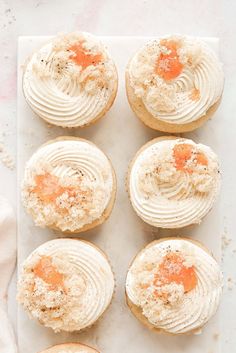 six cupcakes with white frosting and orange sprinkles on top