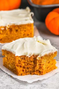 two pieces of pumpkin cake with white frosting on top and an orange in the background