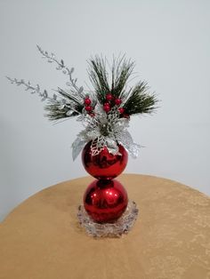 a red vase filled with flowers and greenery on top of a round wooden table