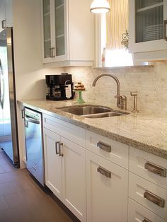 a kitchen with white cabinets and marble counter tops