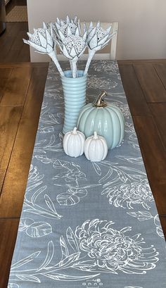 a blue vase filled with white flowers sitting on top of a wooden floor next to a table