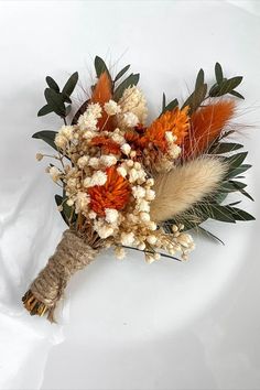 an arrangement of dried flowers and leaves on a white surface