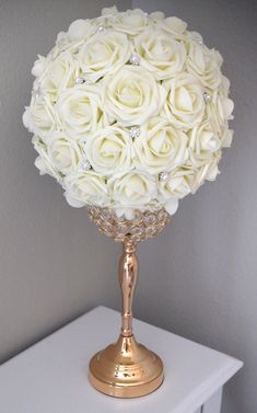 a gold vase filled with white roses on top of a table next to a wall