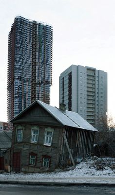 an old wooden building with snow on the ground and tall buildings in the backround