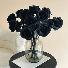 there is a vase with black roses in it sitting on a table next to a white chair