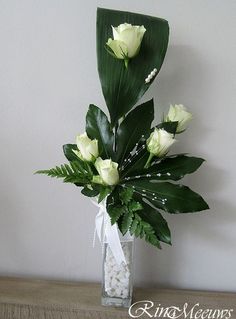 a vase filled with white flowers and greenery on top of a wooden table next to a wall