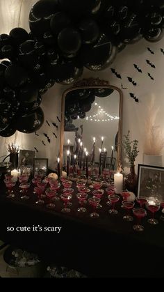 a table topped with lots of black balloons and candles next to a wall filled with bats