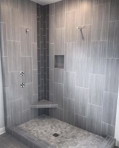 a walk in shower sitting next to a tiled wall and floor covered in gray tiles