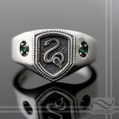 a signet ring with a snake on the front and green stones in the middle