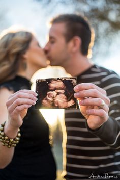 a man and woman kissing while holding up a photo