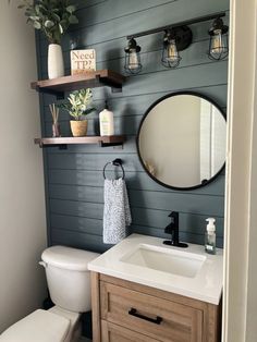 a white toilet sitting next to a bathroom sink under a round mirror on a wall