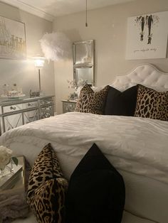 a white bed topped with lots of pillows next to a night stand and mirror cabinet