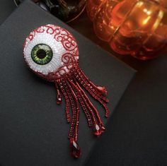 an eyeball brooch with red beads and green eyes sits on a black surface