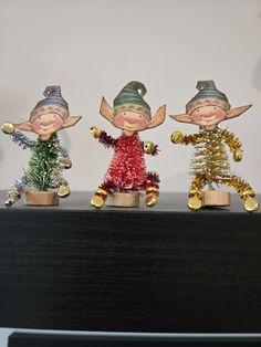 three little christmas elves standing next to each other on top of a shelf in front of a computer monitor