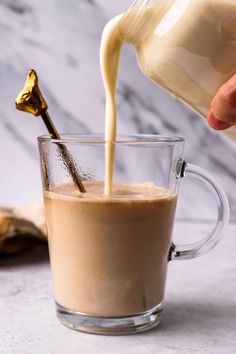 a person pouring milk into a glass mug filled with coffee and banana slices on the side