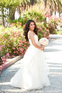 a woman in a white dress holding a bouquet of flowers and posing for the camera