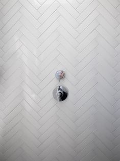 two faucets on the wall in a bathroom with white tile and herringbone pattern