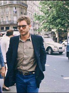 a man and woman walking down the street in front of some cars on a sunny day